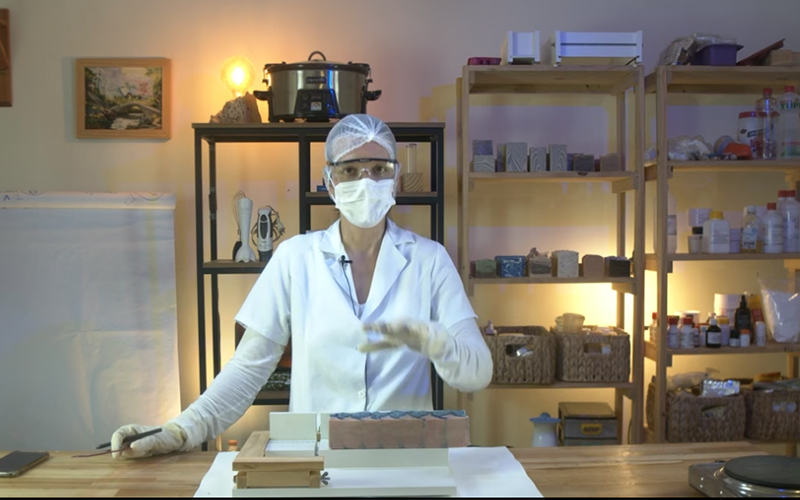 Natália paramentada com jaleco, touca e óculos no primeiro ateliê de produção
