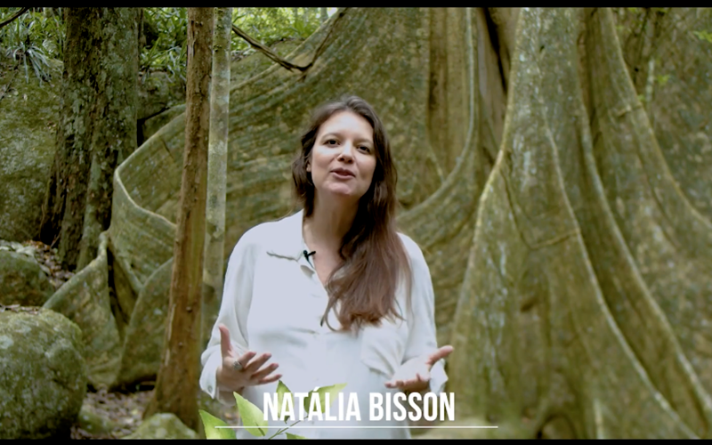Natália Bisson gravando em meio à mata, falando sobre matérias-primas naturais