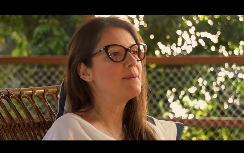 Retrato de Natália Bisson em conversa, ao ar livre, em meio ao verde